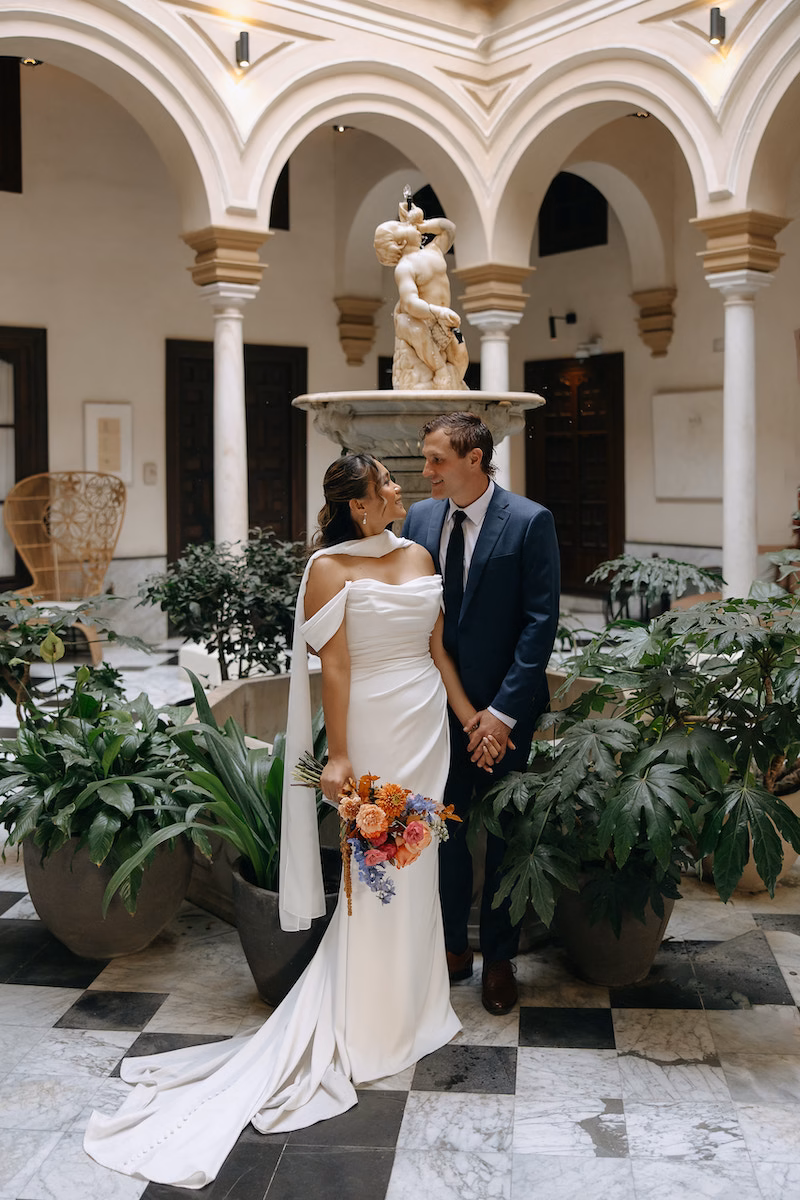 Novios junto a la fuente de mármol en el patio central de CoolRooms Palacio Villapanés, un hotel-palacio del siglo XVIII en Sevilla