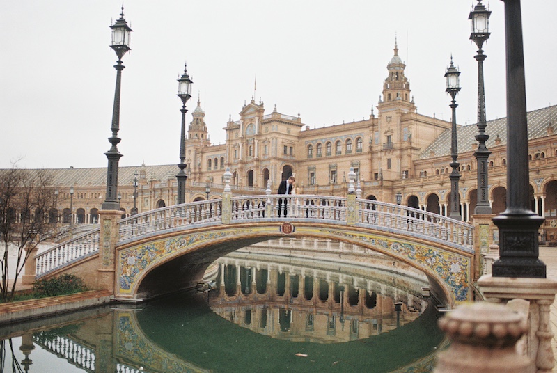Bride and groom standing on the bridge of Plaza de España in Seville during their destination wedding